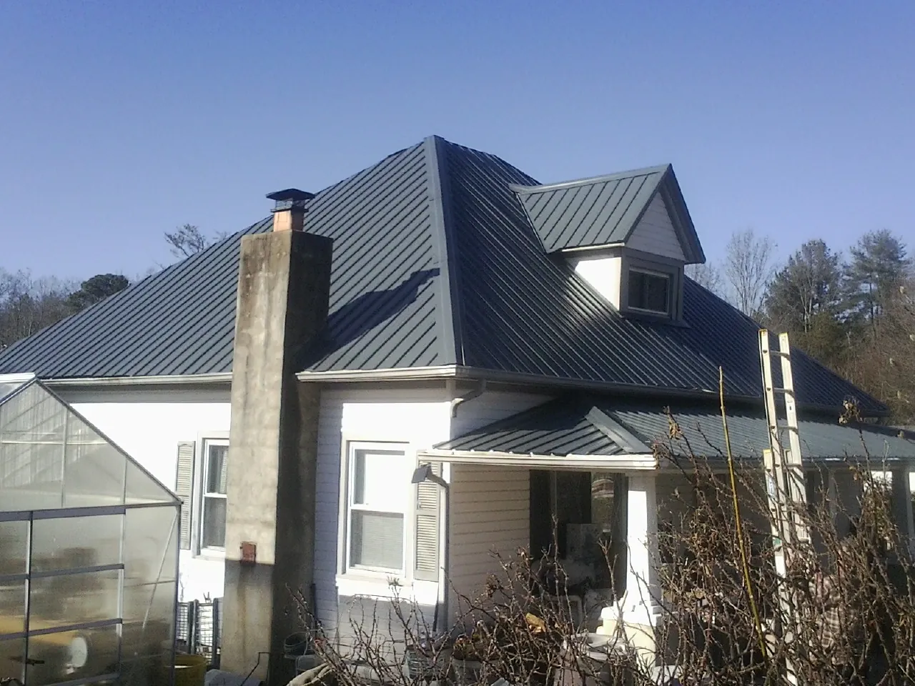 Dark blue standing seam metal roof on a white farmhouse with dormer — Slate & Tile Roof Repair by Roofing Brothers in Roggen