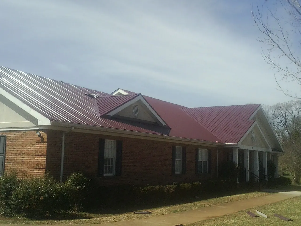 Red metal roof with gabled entries on a long brick building, from a Hail Damage Roof Repair job in Roggen