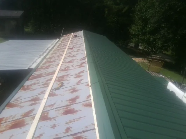 Old rusted panels beside newly installed green metal roofing — Wind Damage Roof Repair by Roofing Brothers in Roggen