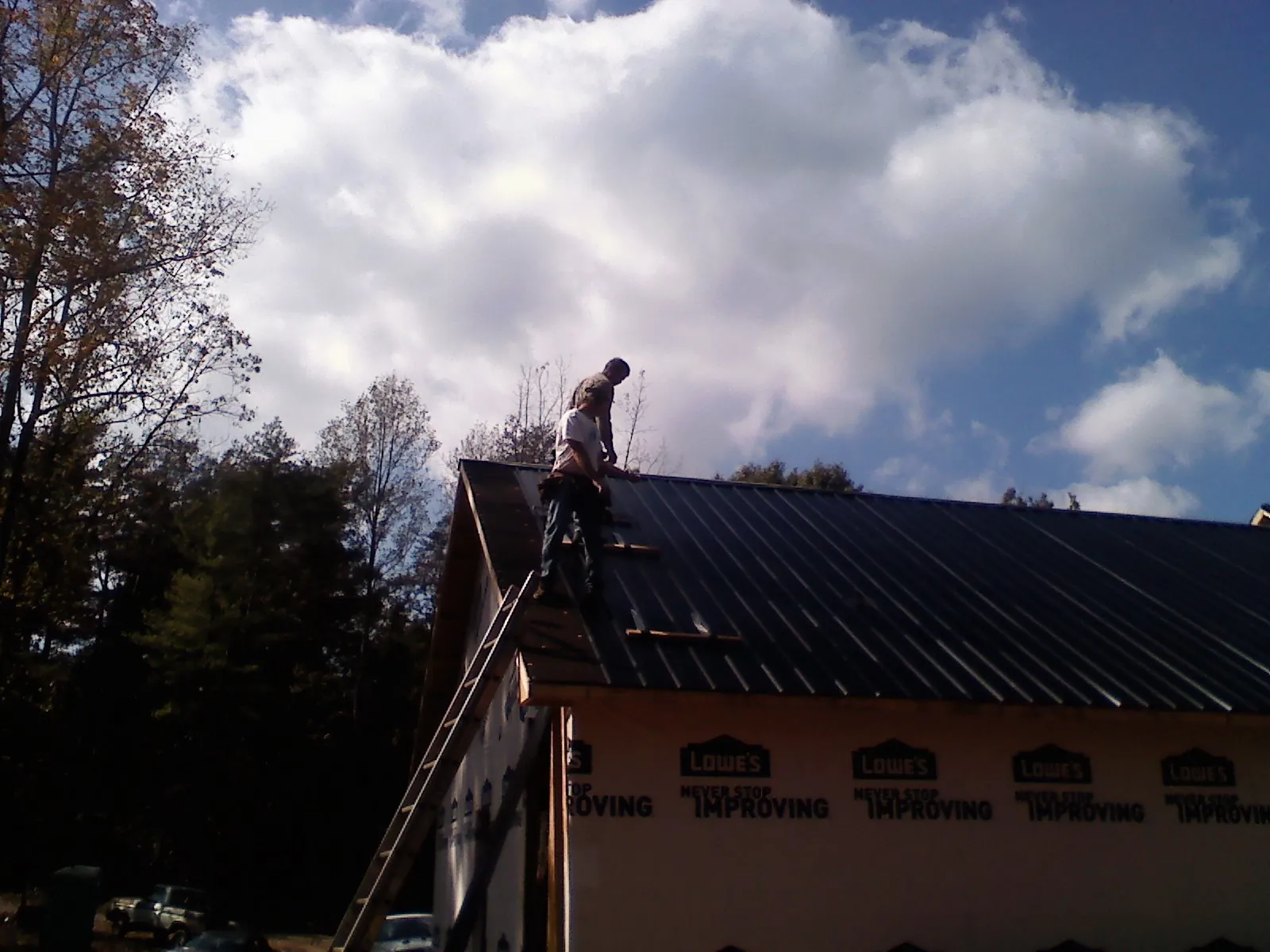 Roofer fastening dark metal panels high against a cloudy sky, from a Roof Inspection job in Roggen