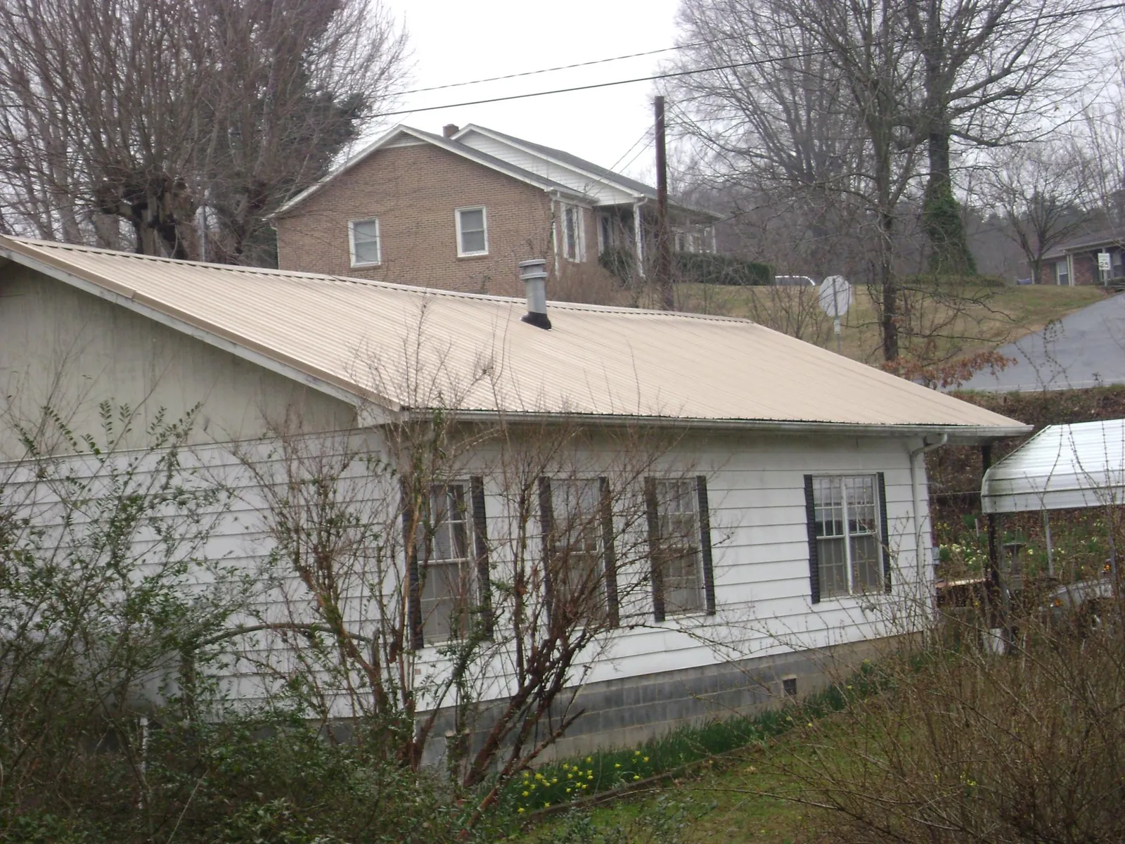 Tan metal roof on a white sided house set into a hillside — Commercial Roofing by Roofing Brothers in Roggen